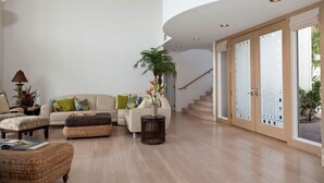 A spacious living room with a high ceiling, a staircase leading to an upper floor, and a large sliding glass door. -  Access to Mauna Lani Spa/Tennis/Pickleball/Gym/Lap Pool included with booking (Waimea)