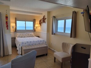 Une chambre à coucher comprenant un lit, deux tables de chevet, une chaise, un téléviseur et des fenêtres avec des rideaux.