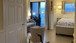 A hotel room with a balcony, a bed with a star-patterned duvet, a seating area with a chair and a table, and a view of the sea.