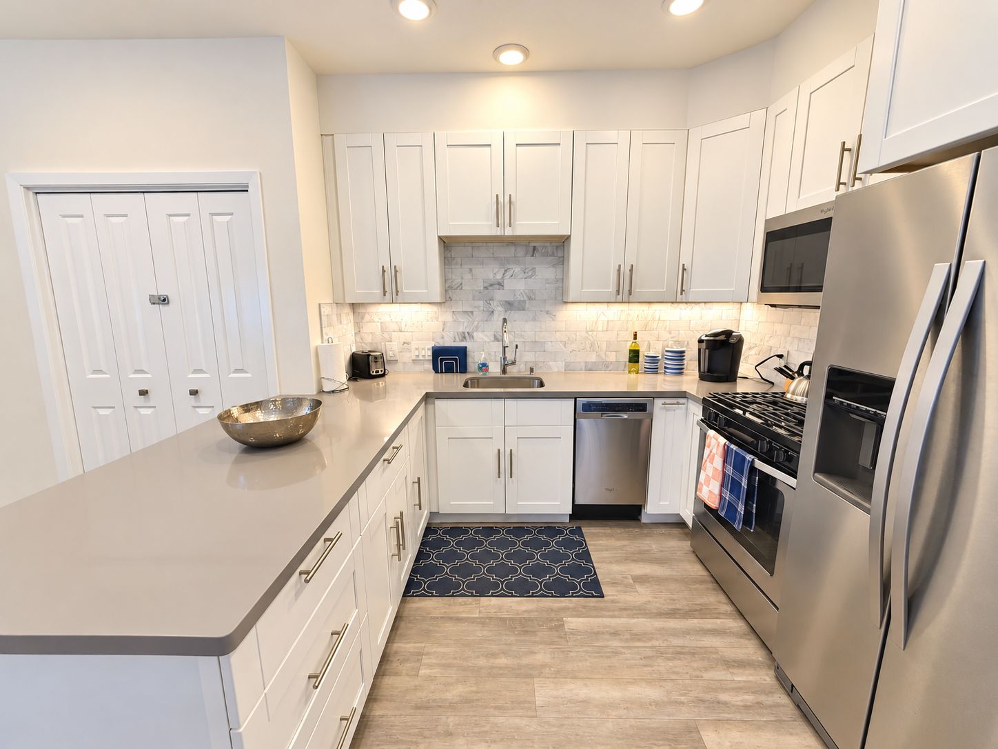 A modern kitchen with white cabinets, stainless steel appliances, and a marble backsplash.