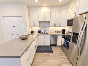 A modern kitchen with white cabinets, stainless steel appliances, and a marble backsplash.