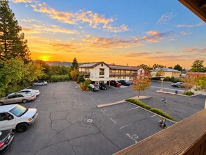 A parking lot with several cars, a building with a flat roof, and a sunset in the background.