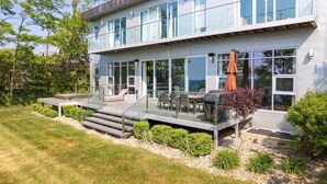 A modern two-story house with a glass balcony, outdoor seating, and a well-maintained garden.