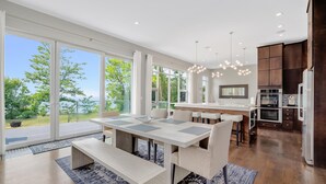 A modern kitchen with large windows, a dining area with a long table, and a view of the outdoors.