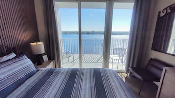 A hotel room with a large bed, a desk, a chair, and a balcony with a view of the sea.