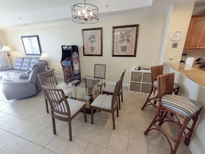 A living room with a glass-top dining table, wooden chairs, a sofa, a TV, and framed artwork on the walls.