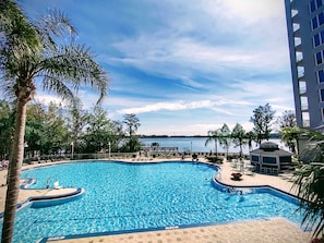 A swimming pool with a view of a body of water, surrounded by palm trees and a building. - DISNEY area CONDO 2 KING BEDS 2 BUNKS 2 BATHS Large 1350 sq ft Lake View 10th fl (Orlando)