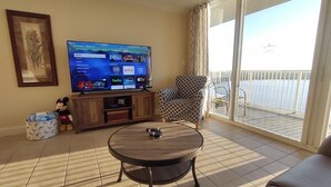 A living room with a flat-screen TV, a patterned armchair, a sofa, and a balcony with a railing. - DISNEY area CONDO 2 KING BEDS 2 BUNKS 2 BATHS Large 1350 sq ft Lake View 10th fl (Orlando)