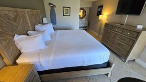 A hotel room with a large bed, a wooden headboard, a bedside table, a dresser, a mirror, a TV, and a lamp. - Right on the Waterfront Marina - Suite 117 - 7150 N Tamiami Tail, Sarasota FL (Sarasota)