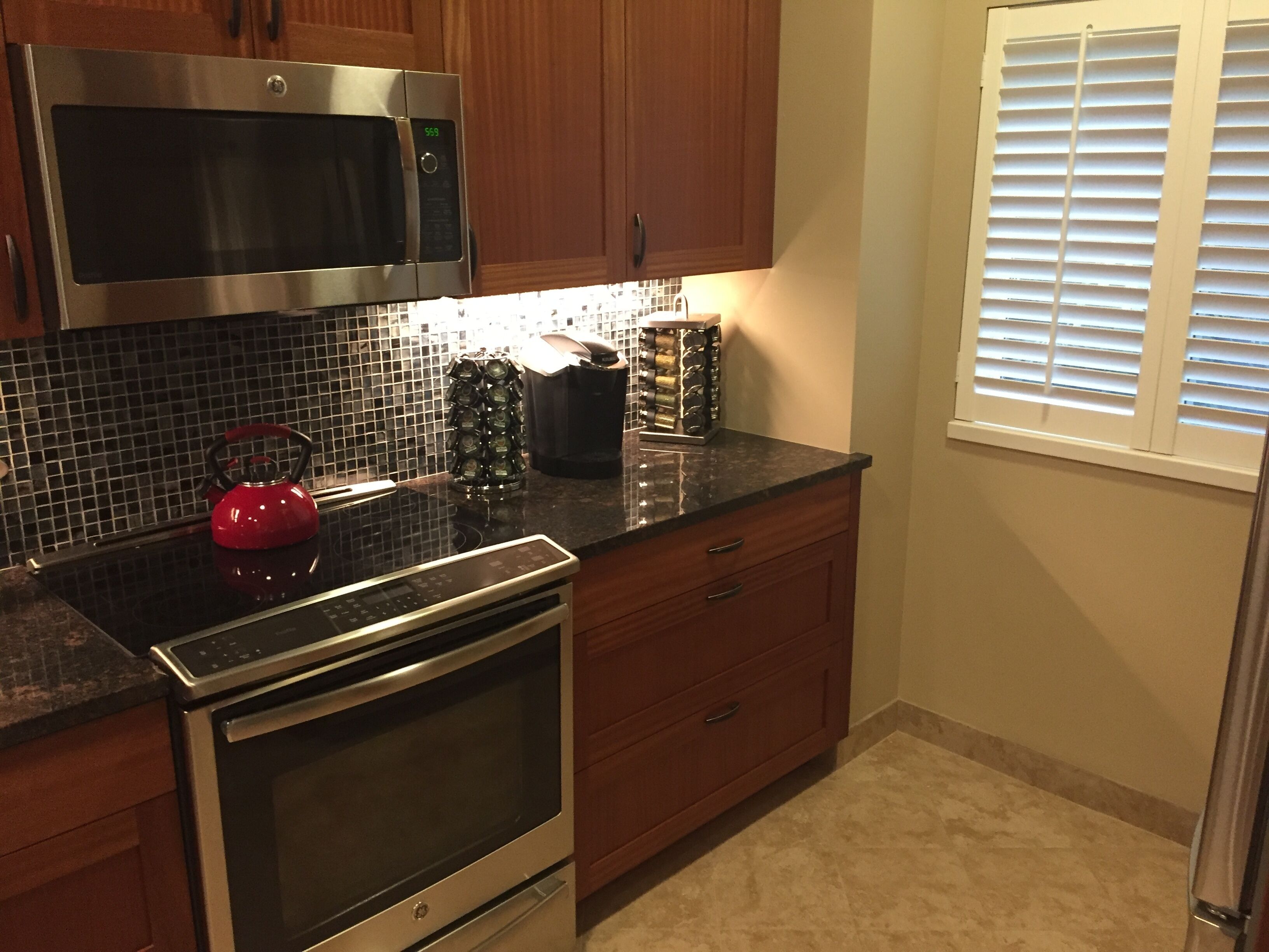A kitchen with a stainless steel microwave, a red kettle, and a coffee maker on the counter.