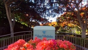 A sign with the text "Vesta International" surrounded by a flower bed with pink and red flowers. - RENOVATED PROPERTY!!  Book now! E101 (Waikoloa)