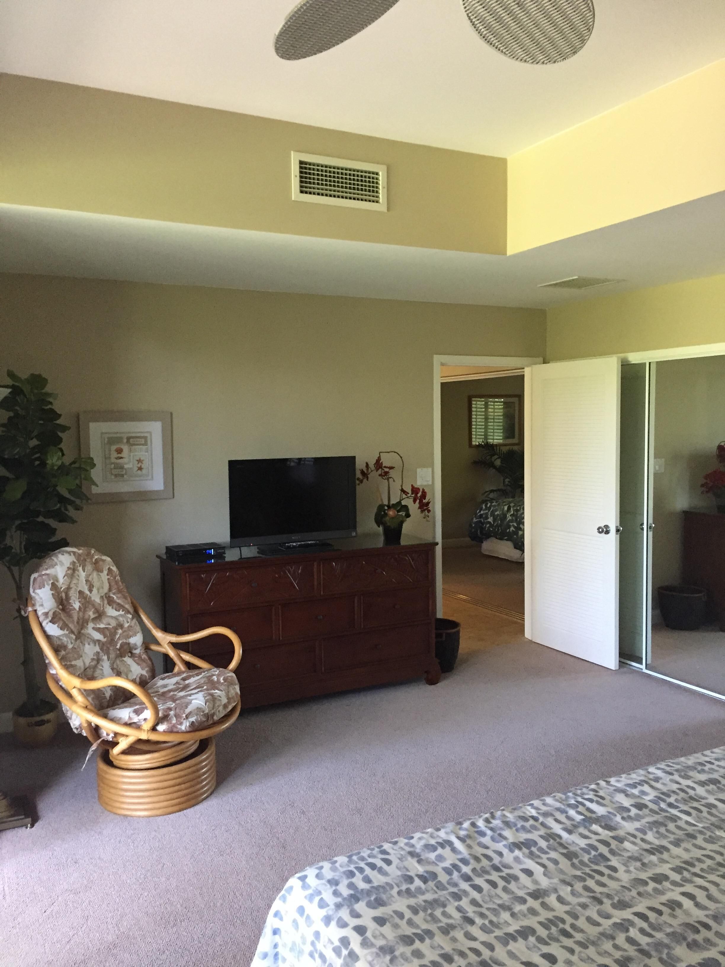 A bedroom with a bed, a television on a wooden dresser, a chair, and a door leading to another room.