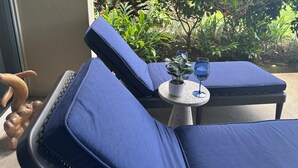A blue cushioned lounge chair with a small table and a potted plant, positioned near a glass of wine. - RENOVATED PROPERTY!!  Book now! E101 (Waikoloa)