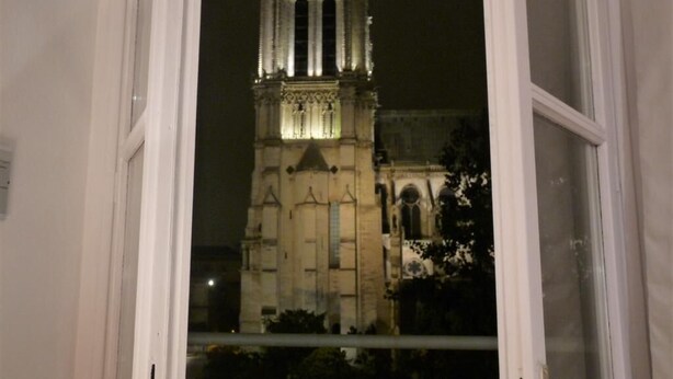 Vista a través de una ventana abierta de un edificio histórico con una torre destacada y ventanas de arco.