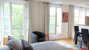 Un dormitorio con cama, una silla, una mesa y ventanas amplias.
