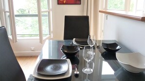 Mesa de comedor servida con platos, tazones y copas de vino, con una silla negra y un cuadro abstracto rojo en la pared.