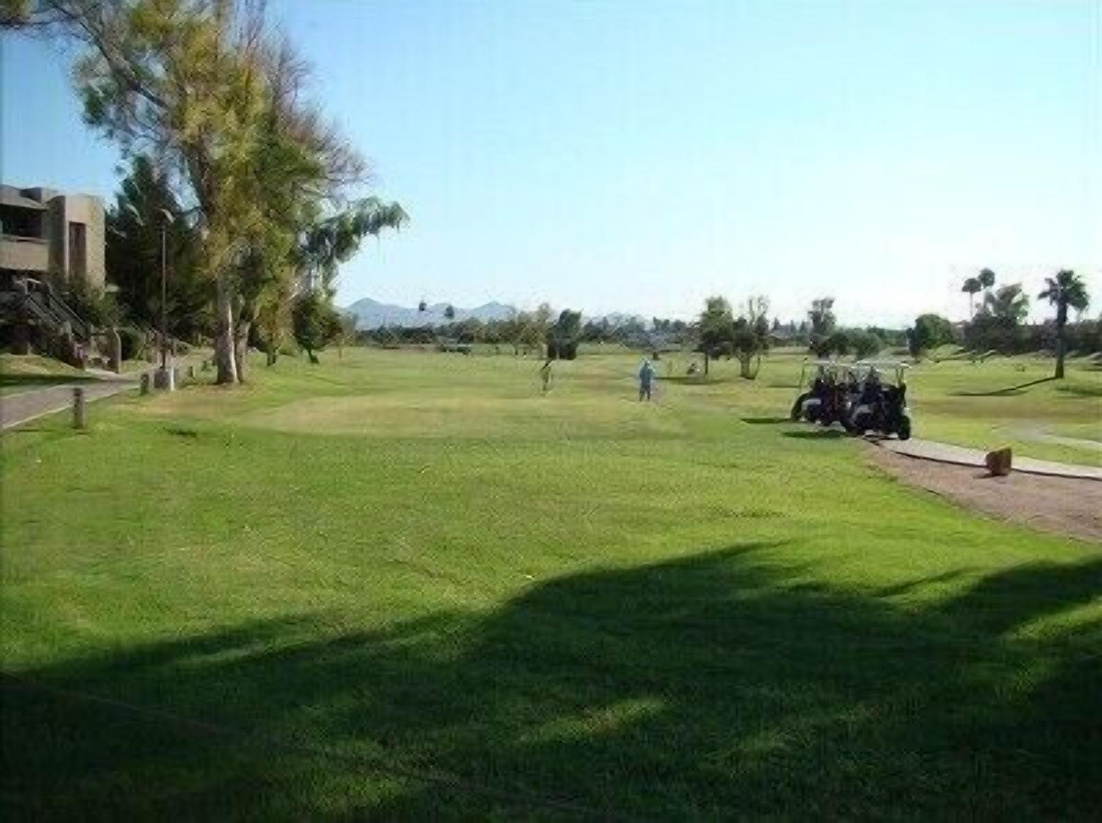 A golf course with a clear path, trees, and a distant mountain range.