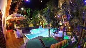 A nighttime pool area with lounge chairs and a thatched umbrella.
