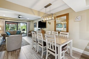 A dining area with a wooden table and white chairs, a ceiling fan, and a large mirror on the wall.