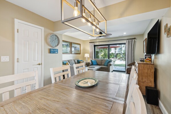 A dining area with a wooden table, chairs, a clock, and a sign indicating a beach direction.