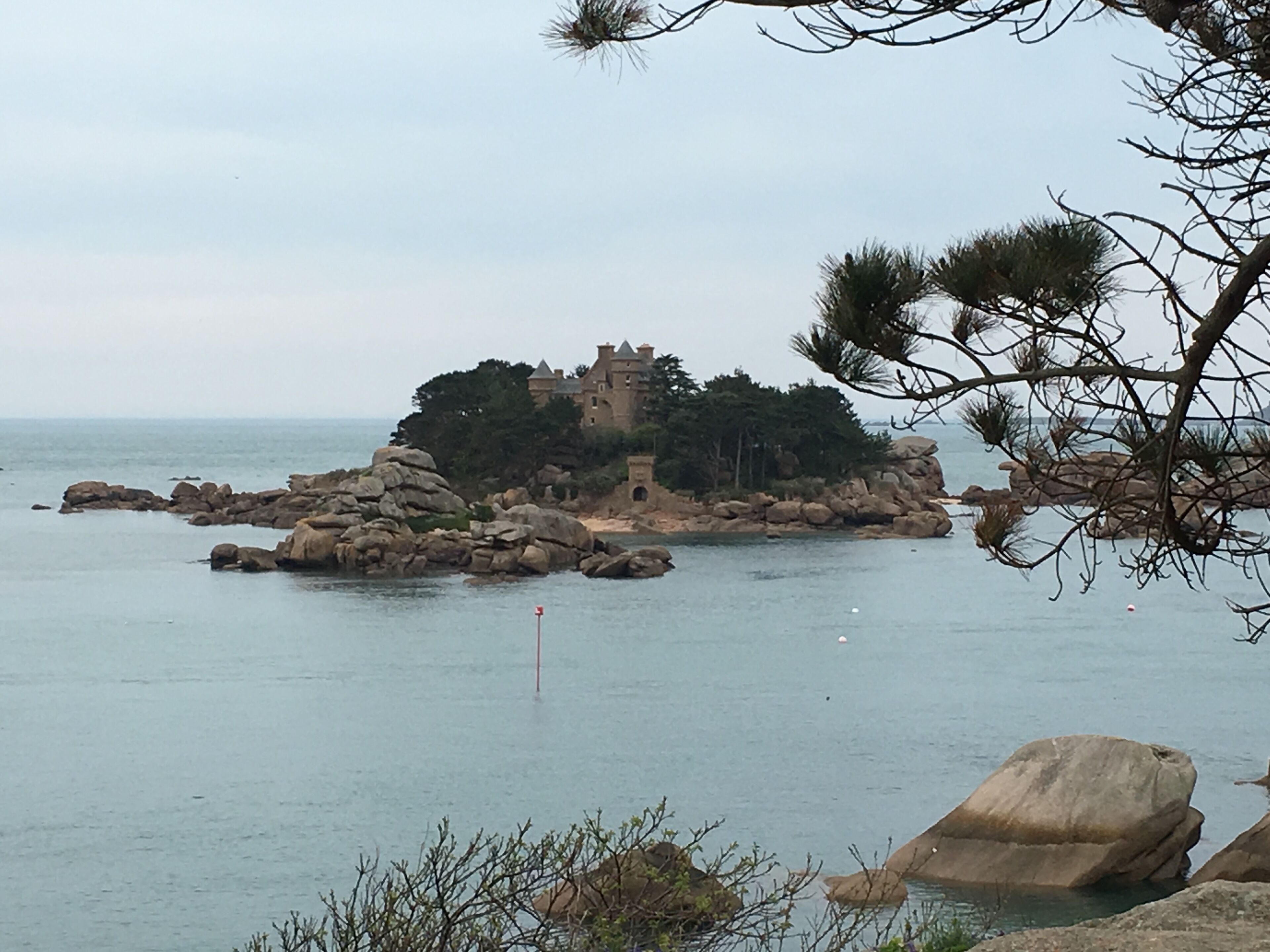 A coastal scene with a castle-like structure surrounded by rocks and trees, overlooking the sea.