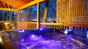 Ett bubbelbad med blått ljus, ett trädäck och ett spaljerstaket.