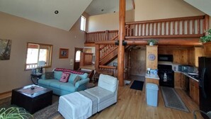 Un espacio habitable amplio con techo alto, una escalera de madera, una cocina y una zona de estar acogedora.
