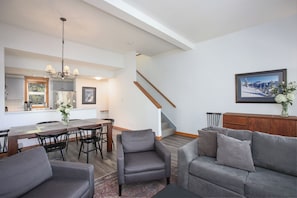 Un salón amplio con una mesa de comedor, sofás grises y una escalera que sube a un nivel superior.