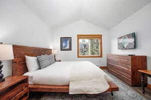 A bedroom with a wooden bed, a nightstand, a dresser, and a window with a view of trees.
