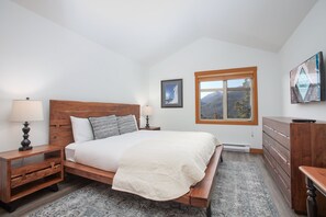 A bedroom with a wooden bed, nightstands, a dresser, and a window with a mountain view.