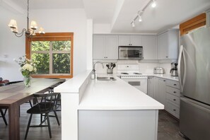 A modern kitchen with white cabinets, stainless steel appliances, and a large island. - Mountain Star 16 - Ski in Walk out, Private Hot Tub, Fireplace (Whistler)
