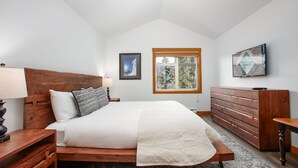 A bedroom with a wooden bed, a nightstand, a dresser, and a window with a view of trees. - Mountain Star 16 - Ski in Walk out, Private Hot Tub, Fireplace (Whistler)