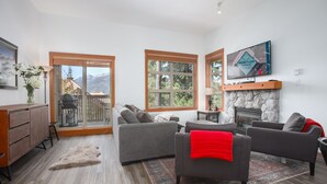 A living room with a fireplace, a television, and a view of the mountains. - Mountain Star 16 - Ski in Walk out, Private Hot Tub, Fireplace (Whistler)