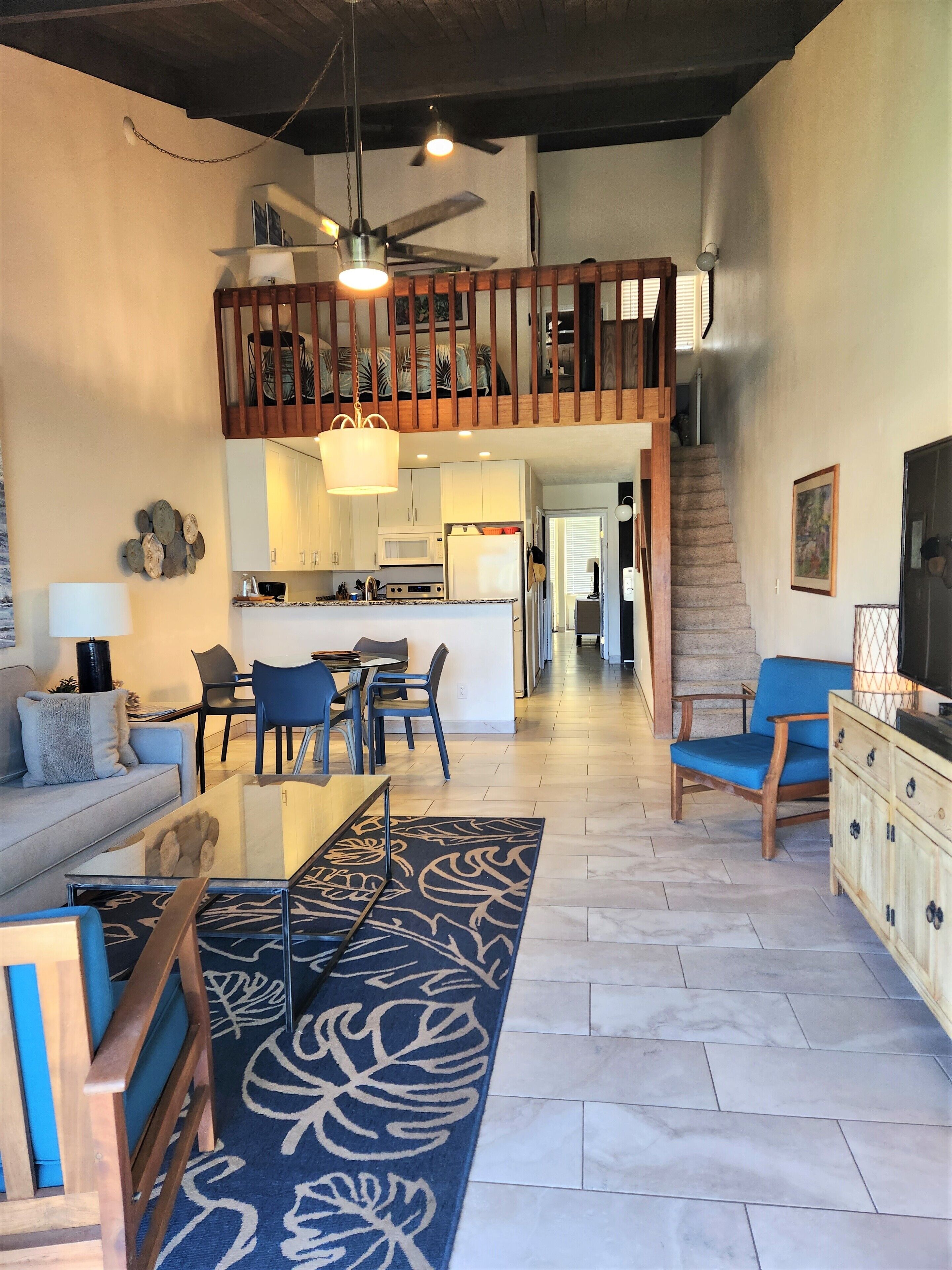 A spacious living area with a high ceiling, a kitchen in the background, and a staircase leading to an upper level.