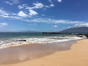 A beach with clear skies, calm waters, and a distant mountain. - Ocean Views | Across from Kamaole III Beach | 1,300+ Sq Ft | Pool | 2 Bed + Loft (Kihei)