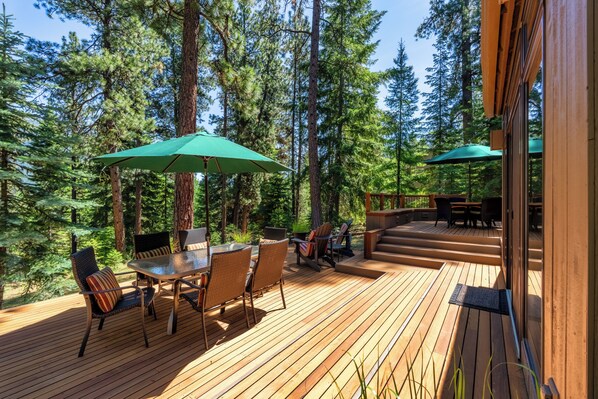 A wooden deck with a dining table and chairs, surrounded by tall trees.