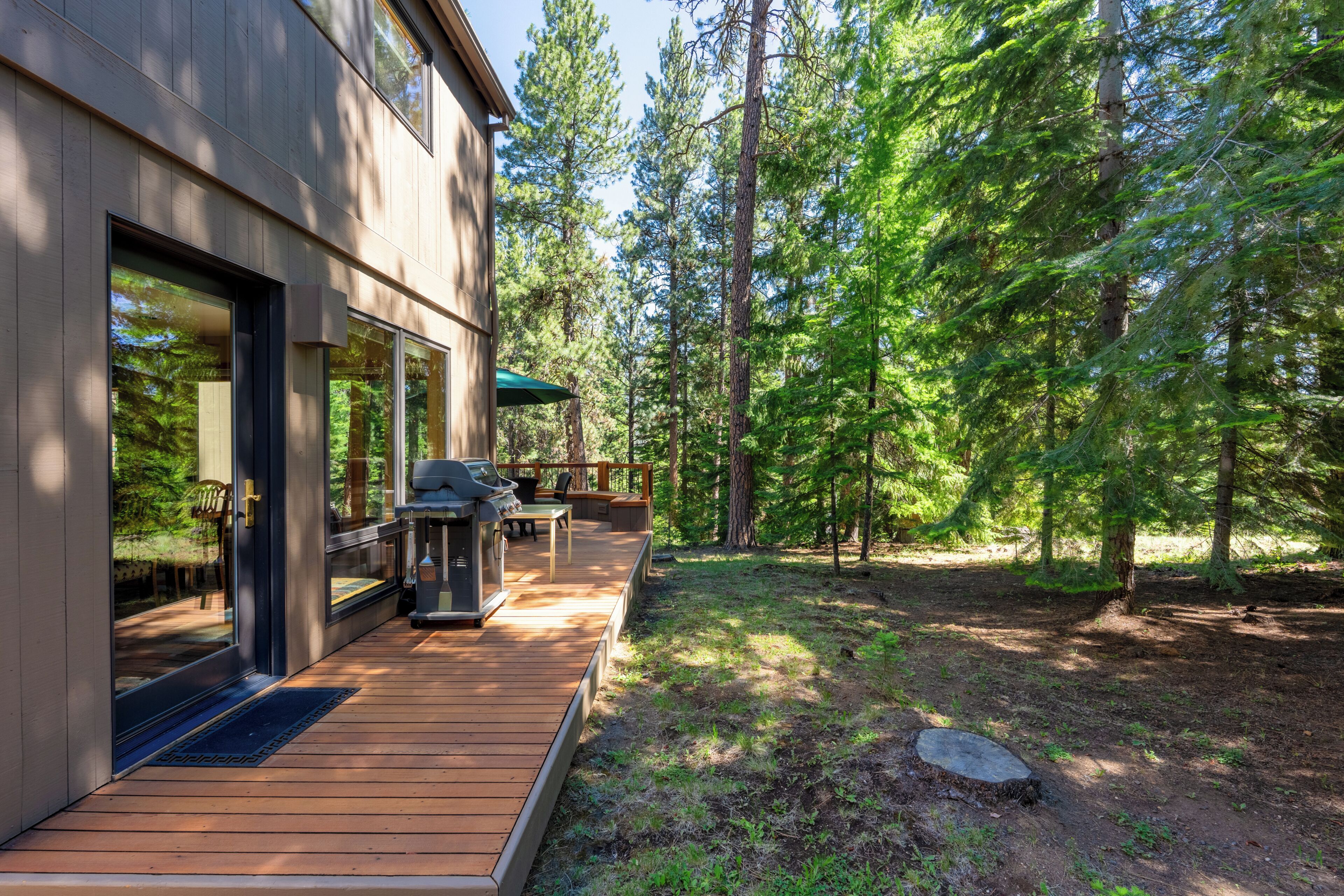 A modern house with a deck, outdoor seating, and a forested backdrop.