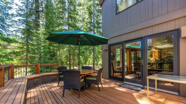 Una terraza de madera con mobiliario exterior, una mesa y una sombrilla.