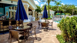 An outdoor bar area with wicker furniture and blue umbrellas, a pool, and lush greenery. - R-disney Palms Retreat -  3 Miles To Walt Disney World (Kissimmee)