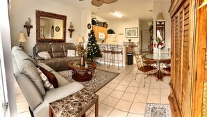 A living room with a sofa, coffee table, and a Christmas tree. There is a dining area with a table and chairs. - R-disney Palms Retreat -  3 Miles To Walt Disney World (Kissimmee)