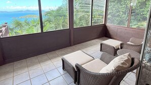 A balcony with wicker furniture, large windows, and a view of the sea. - Bask in Beauty: Anole Offers Unmatched North Shore Views and a Pool Perfect for Relaxation (Cinnamon Bay)