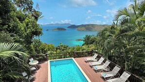 A rectangular pool with a wooden deck, surrounded by lounge chairs and palm trees, overlooking a clear blue sea and distant islands. - Bask in Beauty: Anole Offers Unmatched North Shore Views and a Pool Perfect for Relaxation (Cinnamon Bay)
