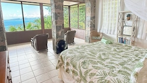 A bedroom with a large bed, a chair, a fan, and a view of the ocean. - Bask in Beauty: Anole Offers Unmatched North Shore Views and a Pool Perfect for Relaxation (Cinnamon Bay)
