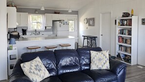 A modern living room with a dark leather sofa, a white coffee table, and a bookshelf filled with books. - Cozy Cottage in Kitty Hawk with Gorgeous Ocean Views! (Kitty Hawk)