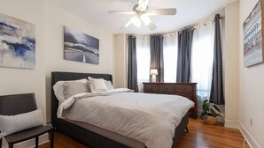 Ein Schlafzimmer mit Bett, Deckenventilator, Nachttisch, Kommode, Sitzbank und einer Topfpflanze.