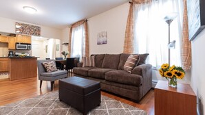 Ein modernes Wohnzimmer mit einer Couch, einem Hocker und einem Essbereich mit Tisch und Stühlen.