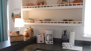 A kitchen with white cabinets, a black countertop, a coffee maker, a toaster, and a set of knives on the counter. - High Hedges Cottage  - Close to downtown Mt Dora in quiet neighborhood (Mt Dora)