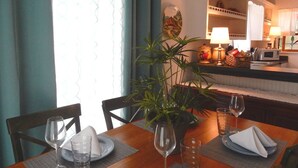 A dining area with a table set for two, a potted plant, and a kitchen in the background. - High Hedges Cottage  - Close to downtown Mt Dora in quiet neighborhood (Mt Dora)