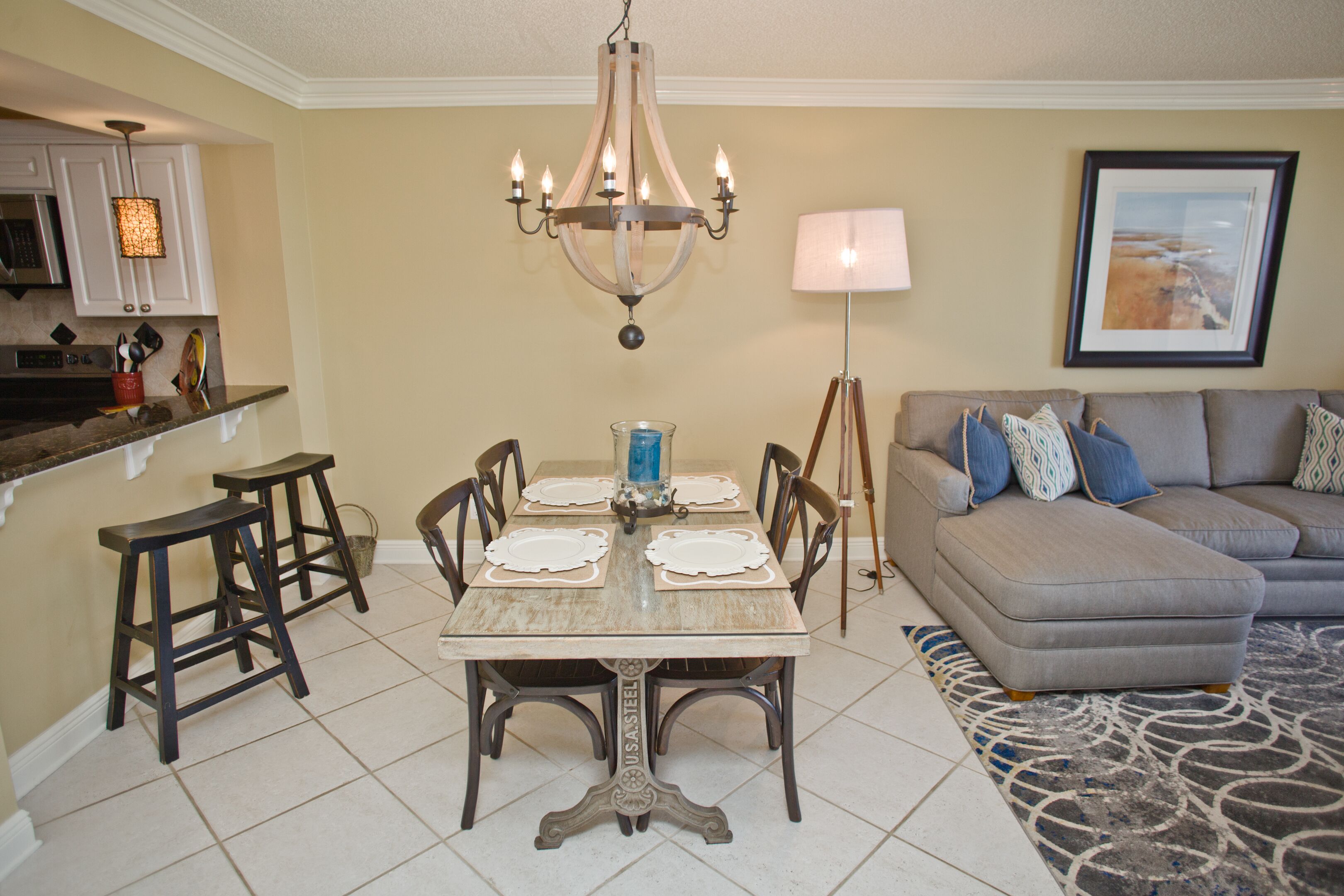 A dining area with a table set for four, a chandelier, and a sofa with patterned cushions.