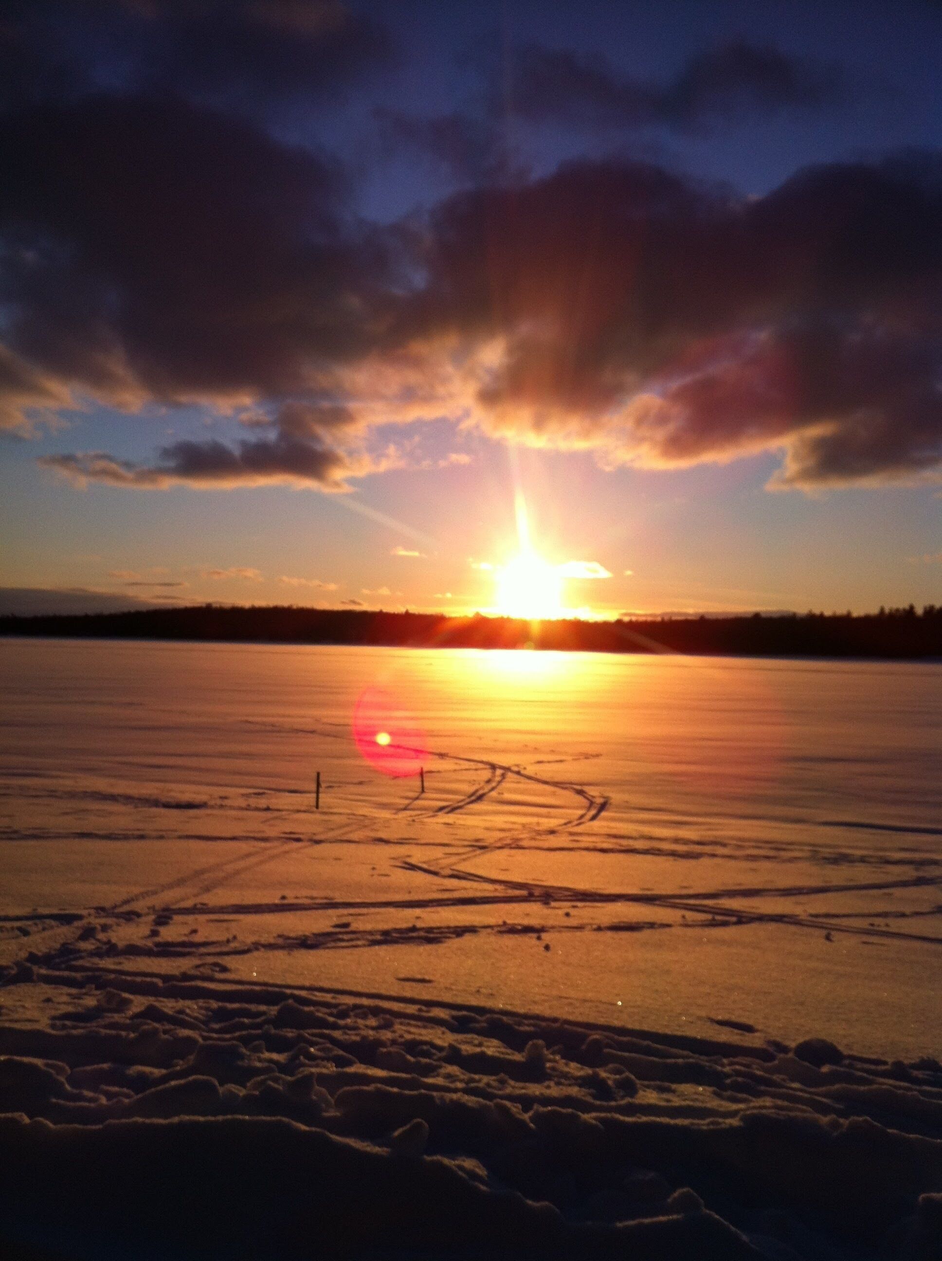 A frozen lake with tracks and a sunset in the background.